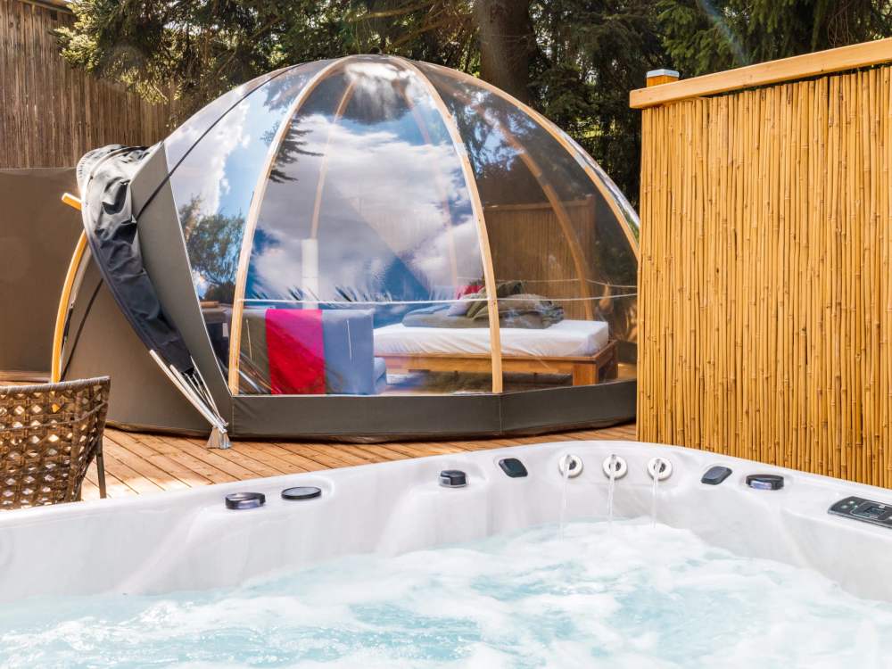 Spa privatif sur la terrasse du Wigwam, avec la tente-bulle et son lit visibles à l'arrière-plan, à La Grange d'Hélène